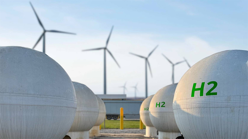 Hydrogen storage tanks marked H2 with wind turbines in the background