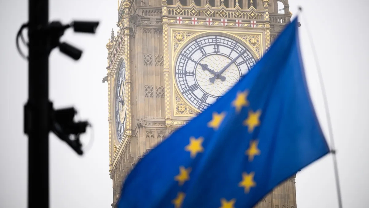 EU flag waving in front of Big Ben with security cameras in view.