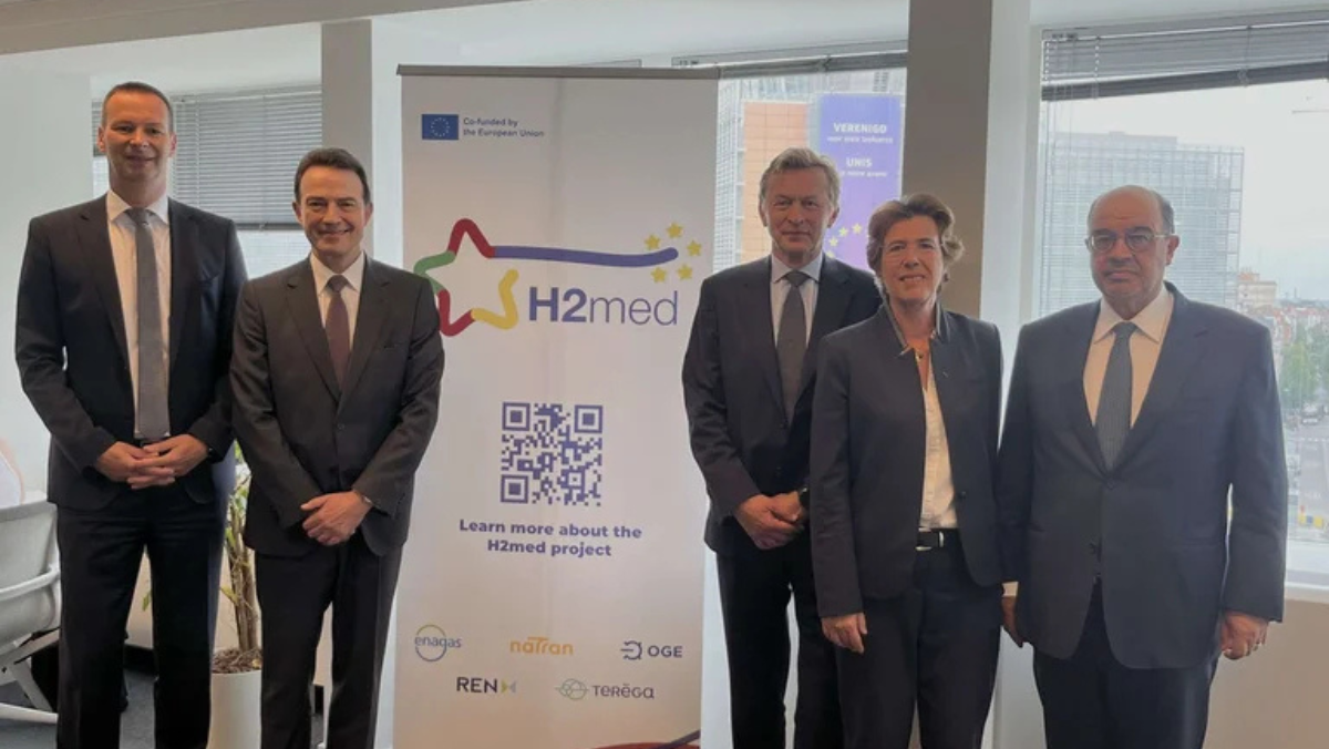 Executives stand beside an H2Med project banner during European hydrogen infrastructure discussions.