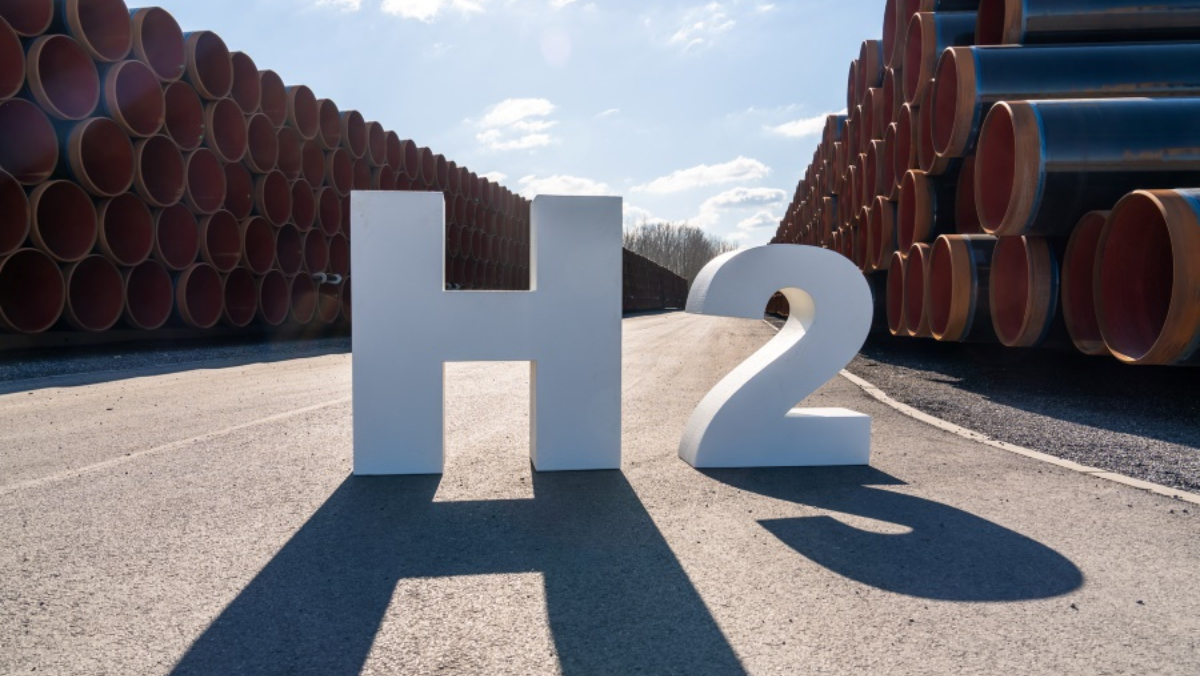 Large H2 sign displayed between stacks of industrial pipeline sections outdoors