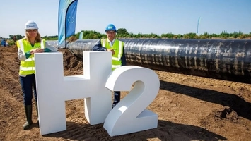 H2 sign at a cross-border hydrogen pipeline site with two professionals in safety gear